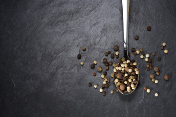 Top view of pepper mix in teaspoon on black slate background.