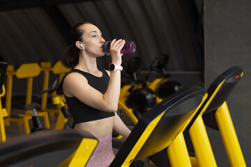 Fototapeta na wymiar Fitness woman drinks a water while runs on treadmill