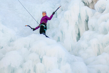 Female ice climber in traction position, swinging ice axes overhead and planting the pick in the ice, side view