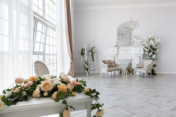 luxurious bright spacious guest room with beautiful chic furniture a huge floor-to-ceiling window in a royal style is decorated with green plants, white walls with stucco and a fireplace