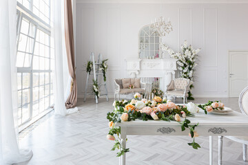 Fototapeta na wymiar luxurious bright spacious guest room with beautiful chic furniture a huge floor-to-ceiling window in a royal style is decorated with green plants, white walls with stucco and a fireplace