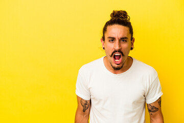 Young caucasian man with long hair isolated on yellow background shouting very angry, rage concept, frustrated.