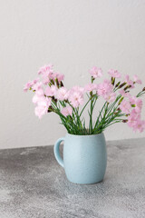 Small pink carnations in a mug on a white wall background, part of a home interior