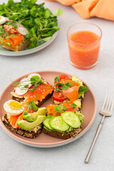 Healthy tasty breakfast, sandwiches with avocado and salmon, cucumbers and tomatoes, radishes and microgreens of peas with boiled egg and root salad, grapefruit smoothie in a glass