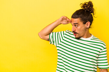 Young caucasian man with long hair isolated on yellow background looking far away keeping hand on...