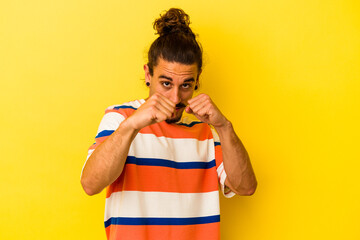 Young caucasian man with long hair isolated on yellow background throwing a punch, anger, fighting due to an argument, boxing.