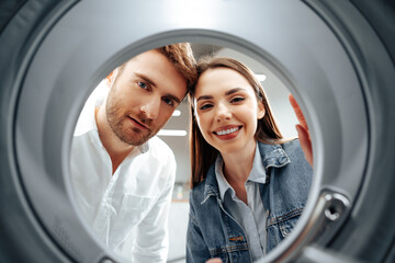 Happy couple choosing new washing machine in a store, view from the inside of washing machine