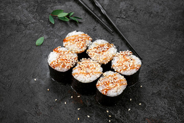 Maki Japanese roll with smoked eel and sesame seeds on stone. Unagi sushi-roll and chopstick