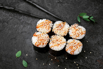 Maki Japanese roll with smoked eel and sesame seeds on stone. Unagi sushi-roll and chopstick, top view, close-up
