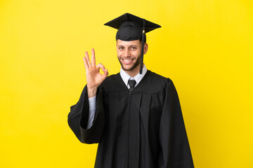 Young university graduate caucasian man isolated on yellow background showing ok sign with fingers