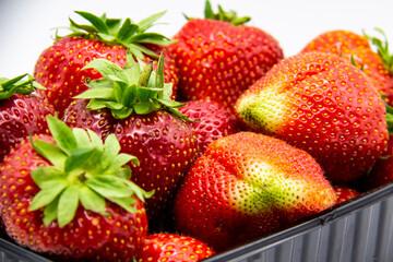 Strawberries in a dark plastic container against white background. Sweet and beautiful berry in a plastic container. Strawberries for sale.