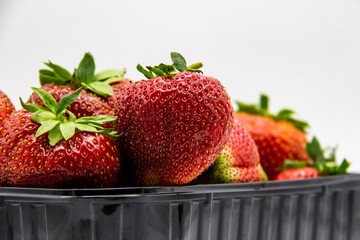 Strawberries in a dark plastic container against white background. Sweet and beautiful berry in a plastic container. Strawberries for sale.