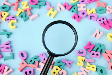 Lots of multicolored wooden letters scattered on a blue background. Magnifying glass in center.