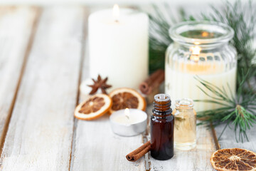 Obraz na płótnie Canvas Assortment of natural christmas essential oils in small bottles. Candles, branches of fir tree. Aromatherapy, cozy home atmosphere, holiday festive mood. Close up macro, wooden background. Zero waste