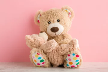 Fototapeten Brown teddy bear mother sitting and holding her baby on table at light pink wall background. Lovely, emotional moment. Closeup. Front view. © fotoduets