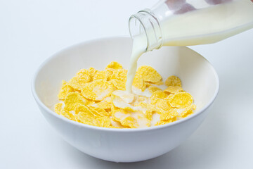 Milk is poured into a plate with cornflakes on a white background. Healthy and tasty breakfast.