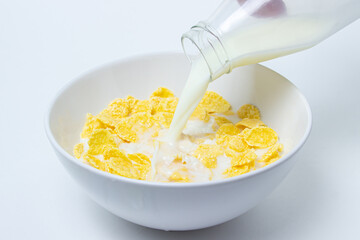 Milk is poured into a plate with cornflakes on a white background. Healthy and tasty breakfast.