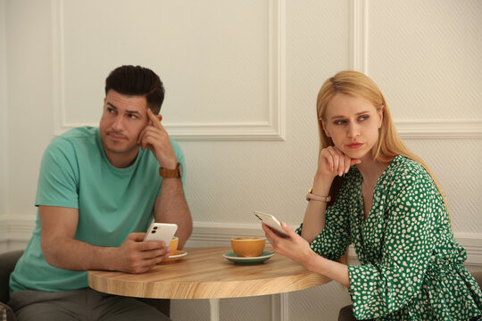 Displeased Man And Young Woman With Smartphones In Cafe. Failed First Date