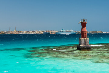 A Red Lighthouse Surrounded by Blue-Green Water Standing in Front of the Port of Hurghada