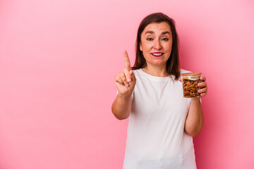 Middle age caucasian woman holding an almond jar isolated on pink background showing number one with finger.