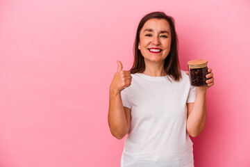 Middle age caucasian woman holding a coffee jar isolated on pink background smiling and raising...