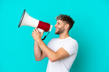 Young handsome caucasian man isolated on blue background shouting through a megaphone to announce...