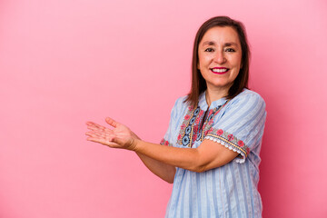 Middle age caucasian woman isolated on pink background holding a copy space on a palm.