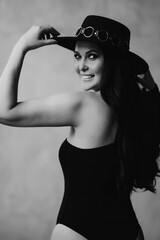 happy and beautiful woman with long dark hair in a black bodysuit and hat. 