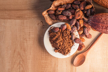 Cocoa powder and cocoa beans with cocoa pods on wooden background.