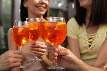 Friends clinking glasses of Aperol spritz cocktails outdoors, closeup