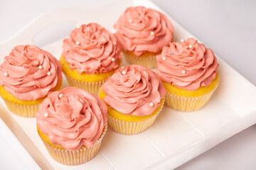 Fresh and delicious cupcakes with yogurt cream. Cakes with cream on table. Muffin with cream. Ready-made pastry, dessert for serving. Indoor studio shot isolated on pink background.