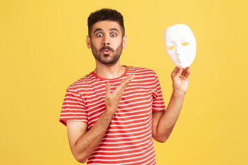 Surprised bearded man pointing at white anonymous face mask looking at camera with astonishment,...