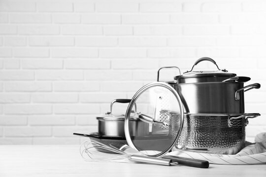 Set Of Clean Kitchenware On White Table Against Brick Wall. Space For Text