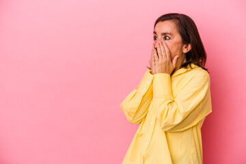 Middle age caucasian woman isolated on pink background thoughtful looking to a copy space covering mouth with hand.