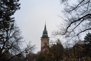 Close up on the clock tower of the Subotica City Hall, in Serbia, at sunset, in autumn, surrounded by trees. Also called Gradska Kuca, it is the main landmark of the city, inaugurated in 1910....