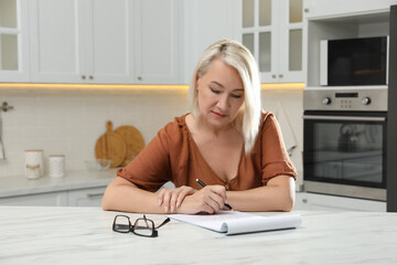 Middle aged woman solving sudoku puzzle at table in kitchen