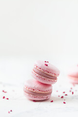 Pink macaroons with shallow depth of field on the white background. French sweet dessert cookies with red crumbs of freeze-dried raspberries lying around.