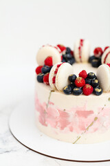 Birthday or anniversary cake with cream cheese frosting decorated with macaroons, blueberries and raspberries. Gold splash on the wedding cake. White background