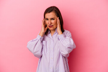 Middle age caucasian woman isolated on pink background covering ears with fingers, stressed and desperate by a loudly ambient.