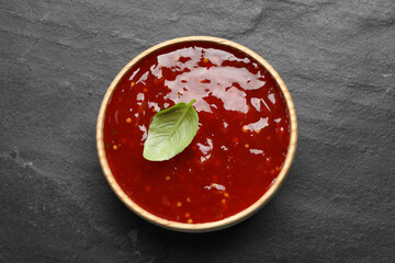 Spicy chili sauce with basil in bowl on black table, top view