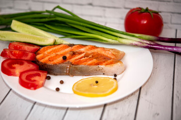 fried piece of salmon on a white plate with tomatoes, onions, cucumbers, on the boards