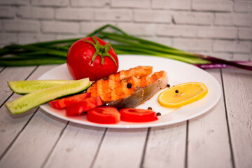 fried fish steak on a white plate with tomatoes, onions, cucumbers, on the boards