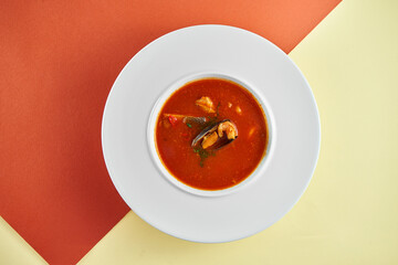 Red tomato soup with seafood, mussels and shrimps in a white plate on colored backgrounds.