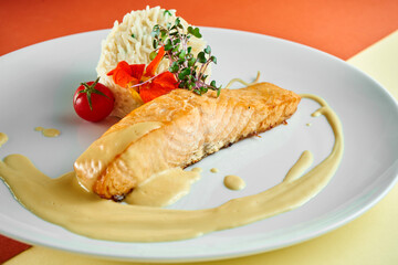 Stir-fried salmon steak with yellow sauce and rice on a side dish in a white plate on colored backgrounds.