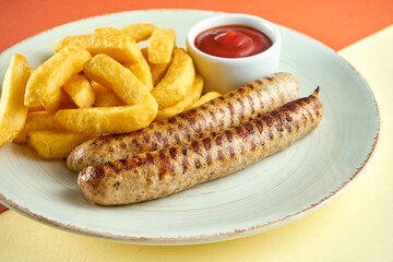 Classic German grilled sausages with French fries and red sauce in a white plate on colored backgrounds.