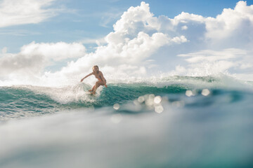 young blonde woman in the bikini doing surfing and smiling with beautiful clouds at the background....