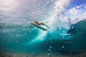 beautiful woman in the bikini doing duck dive with the surfboard under the waves in the clear water with the bubbles 