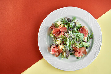 Delicious mix salad with jamon and pear in a white plate on bright colored backgrounds