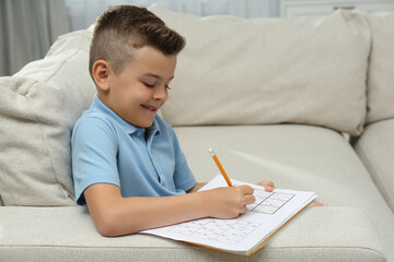 Little boy solving sudoku puzzle on sofa at home