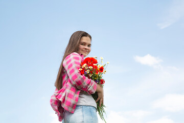 Bouquet of wildflowers: poppies, daisies in hand against the blue sky.